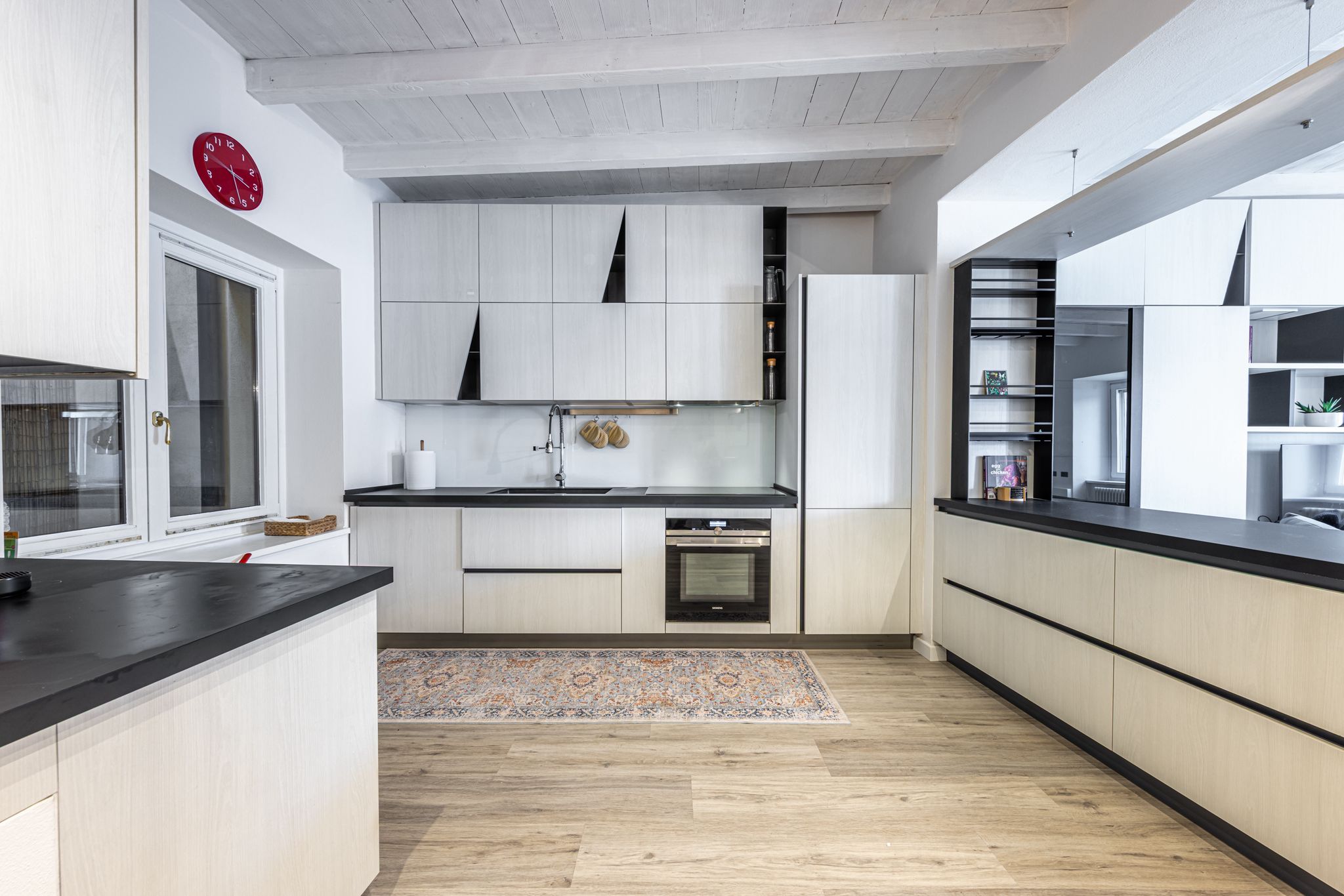 Aqua Vista di Splendore — cucina open-space con isola centrale, orologio rosso vintage e soffitto a travi bianche